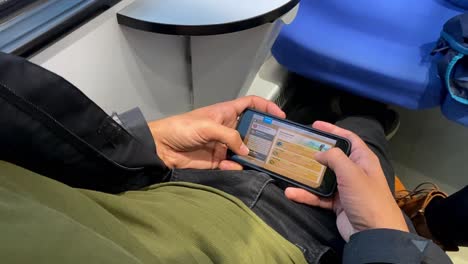 while traveling by train in bari, italy, a man enjoys playing a video game on his mobile device