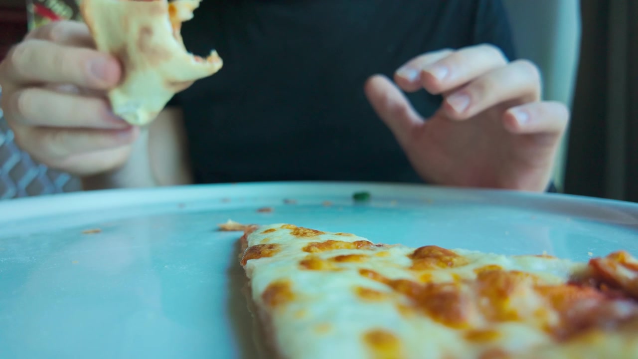 Uomo che mangia lentamente pizza al salame, illustrando un'alimentazione non sana e l'aumento dell'obesità.