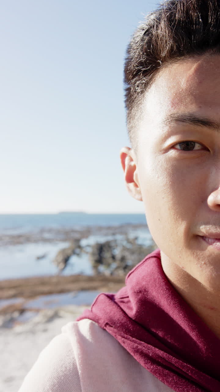 Slow-motion vertical video of joyful Asian man by the sea, looking at camera