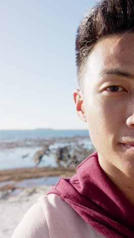 slow-motion vertical video of joyful asian man by the sea, looking at camera