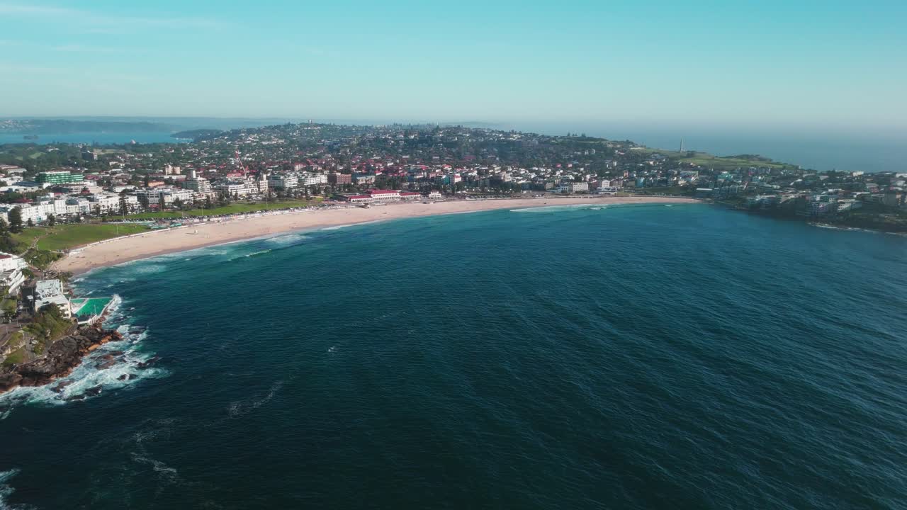 imágenes expansivas de drones de la playa de bondi con sus arenas doradas, la piscina de icebergs y el vibrante suburbio costero bajo cielos azules soleados. capturado en 4k a 25 fps, destacando la icónica costa de sídney.