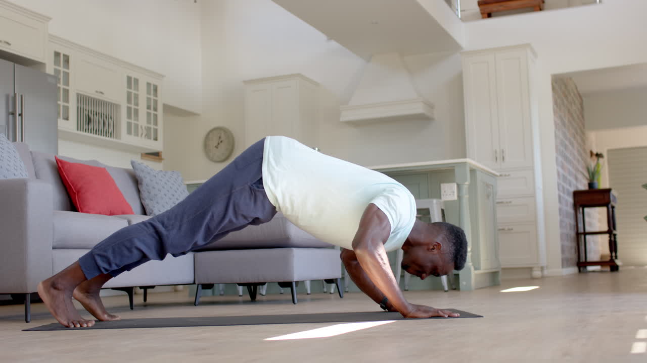 un hombre afroamericano concentrado haciendo flexiones en una sala de estar soleada, en cámara lenta.