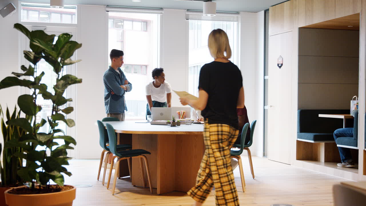 큰 사무실 공간에서 테이블을 둘러싼 창의적 인 팀 회의에 문서와 함께 걸어가는 동료