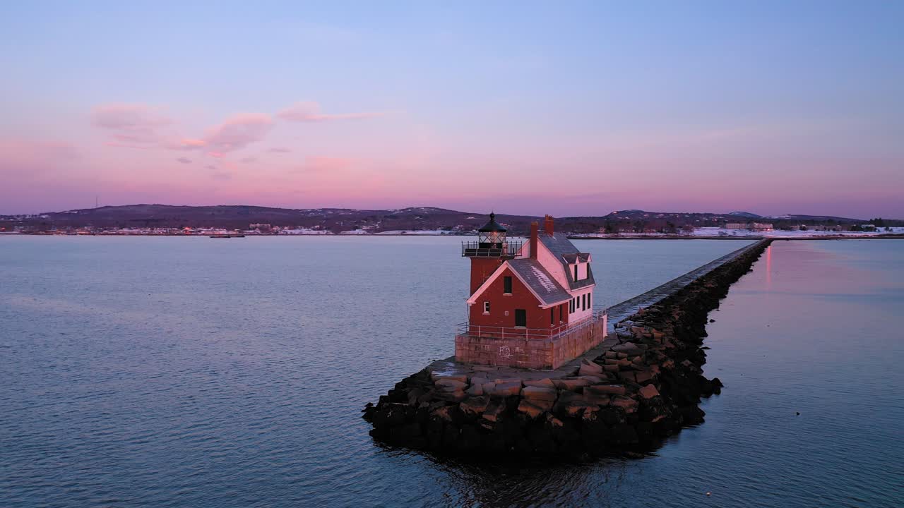 설정 보름달에서 멀리 눈 먼지 바위 방파제 끝에 붉은 벽돌 등대 주변의 낮은 공중 궤도