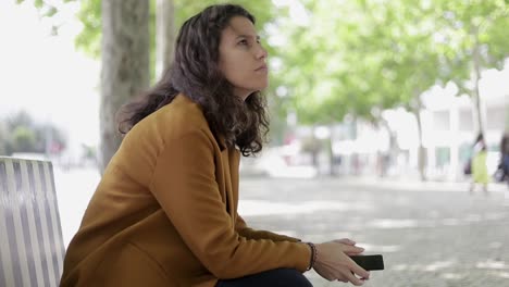 Pensive-girl-with-smartphone-sitting-outdoor