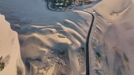 Oasis-Del-Desierto-Huacachina,-Perú-Con-Lago-Y-Palmeras,-Con-Grandes-Dunas-De-Arena-En-El-Fondo