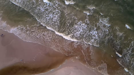 waves breaking on shore of seaside village karwia in poland, top down aerial