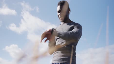 hombre afroamericano bebiendo agua mientras hace ejercicio en el campo comprobando su reloj