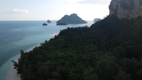 Many-green-trees-with-tall-palm-beans-between-the-high-rocks-and-a-beautiful-view-of-the-clear-blue-sea-on-a-sunny-day-at-Ko-Poda-Beach