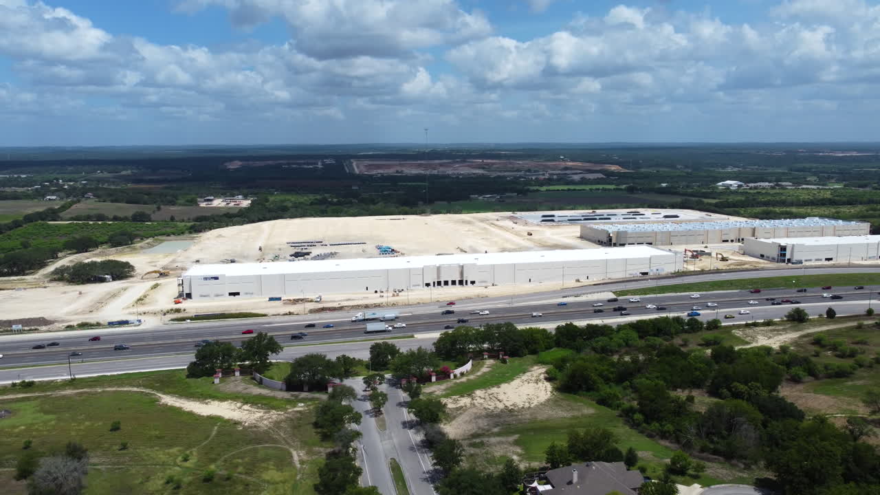 A drone shot captures a highway with the ongoing construction of a large facility in the background, showcasing the bustling activity and infrastructure development.