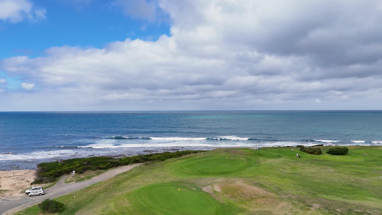 Drone footage captures a scenic golf course by the ocean under partly cloudy skies, highlighting lush greens and coastal beauty