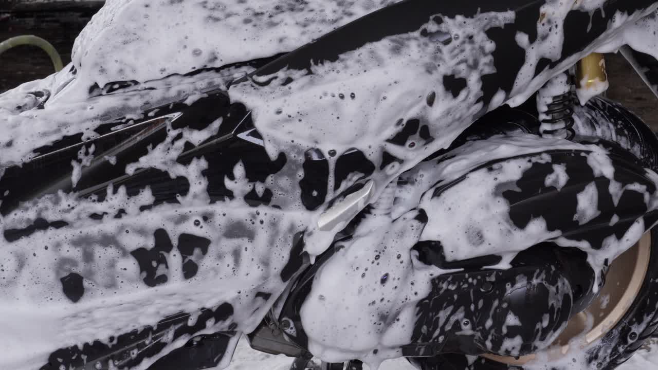Black sleek motorbike, washing chores, soapy suds, close-up view