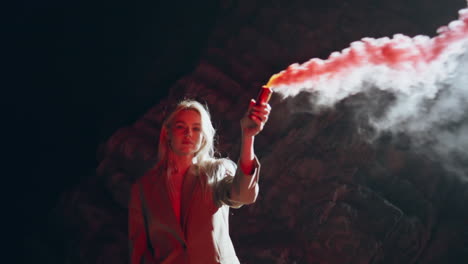 con una bomba de humo feminista en una playa oscura. chica segura mirando a la cámara en el humo