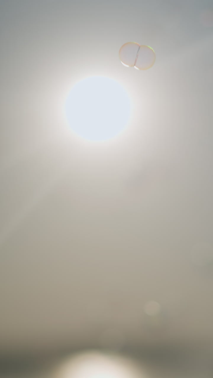 밝은 빛 아래 공중에 부드럽게 떠다니는 거품의 부드럽고 에테리얼한 장면. 빛은 조용하고 꿈 같은 분위기를 만니다.