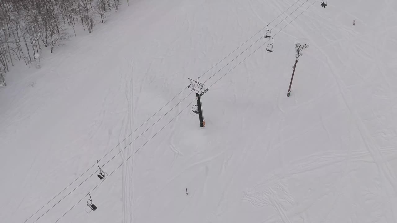 Stationary perspective shot of a ski lift carrying skiers to the top of a mountain in Hokkaido, Japan.