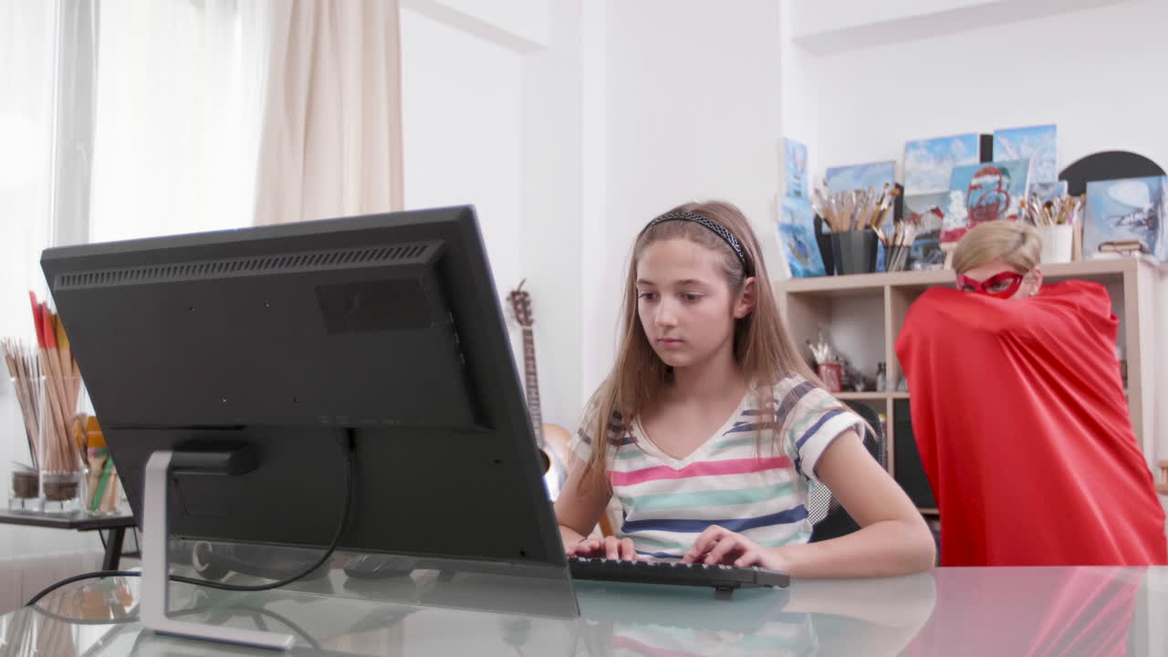 Teenage girl using computer with superhero mother in the background