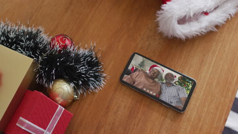 una pareja afroamericana de alto nivel sonriente con sombreros de santa en una videollamada de navidad en un teléfono inteligente