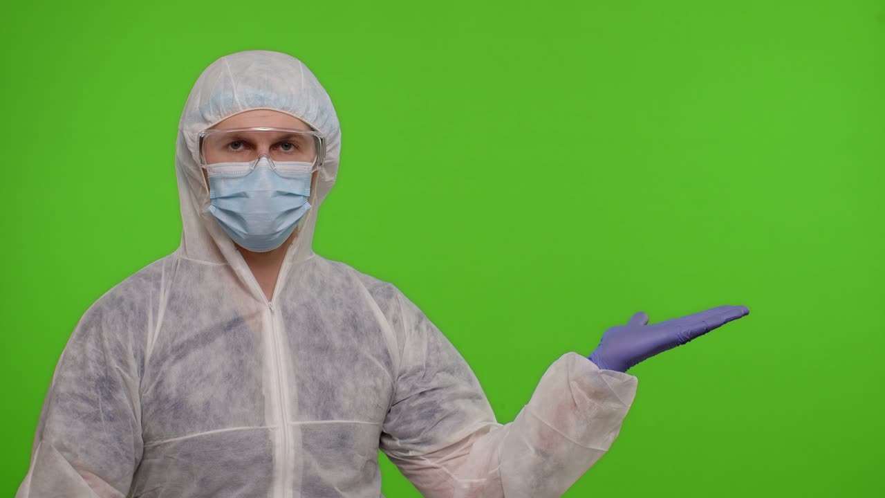 Medical doctor in protective PPE suit pointing at right on blank space on chroma key background