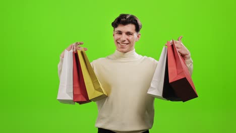 el hombre está de pie y mirando a la cámara. está sonriendo y sosteniendo las bolsas de compras. está de pie sobre un fondo verde. pantalla verde. 4k.
