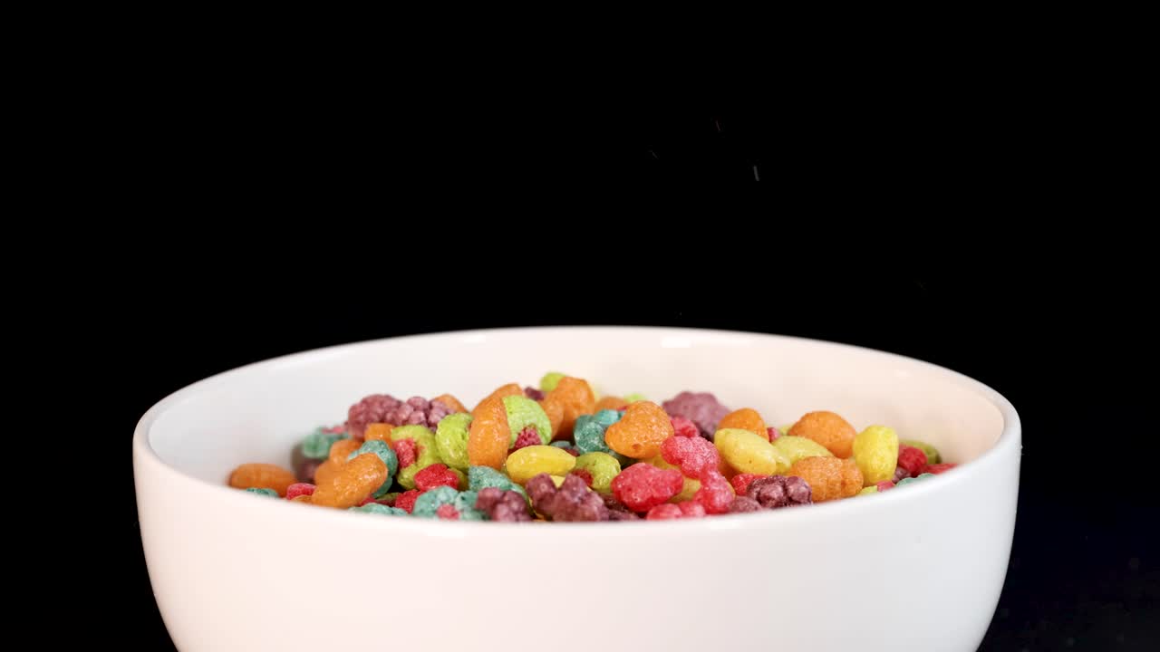 Vibrant cereal pieces cascade into a white bowl against a dark backdrop, creating a dynamic and colorful visual effect