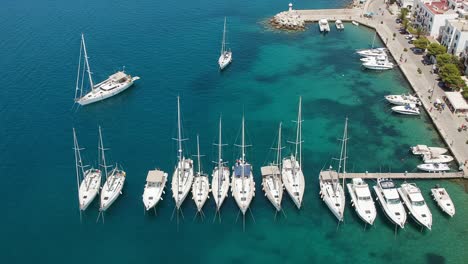 aerial view of a busy marina with sailboats docking and departing from the waterfront, showcasing clear blue waters and scenic coastal landscape