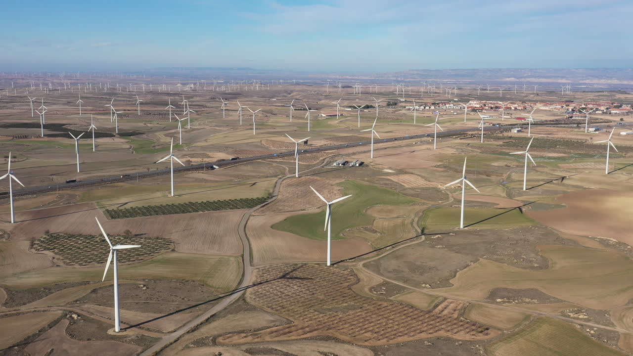Road in the middle of fields with wind turbines sunny day Spain aerial shot