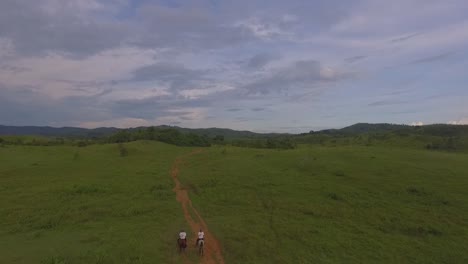 Two-riders-galop-by-a-red-dirt-path-in-a-venezuelan-plain,-slow-motion