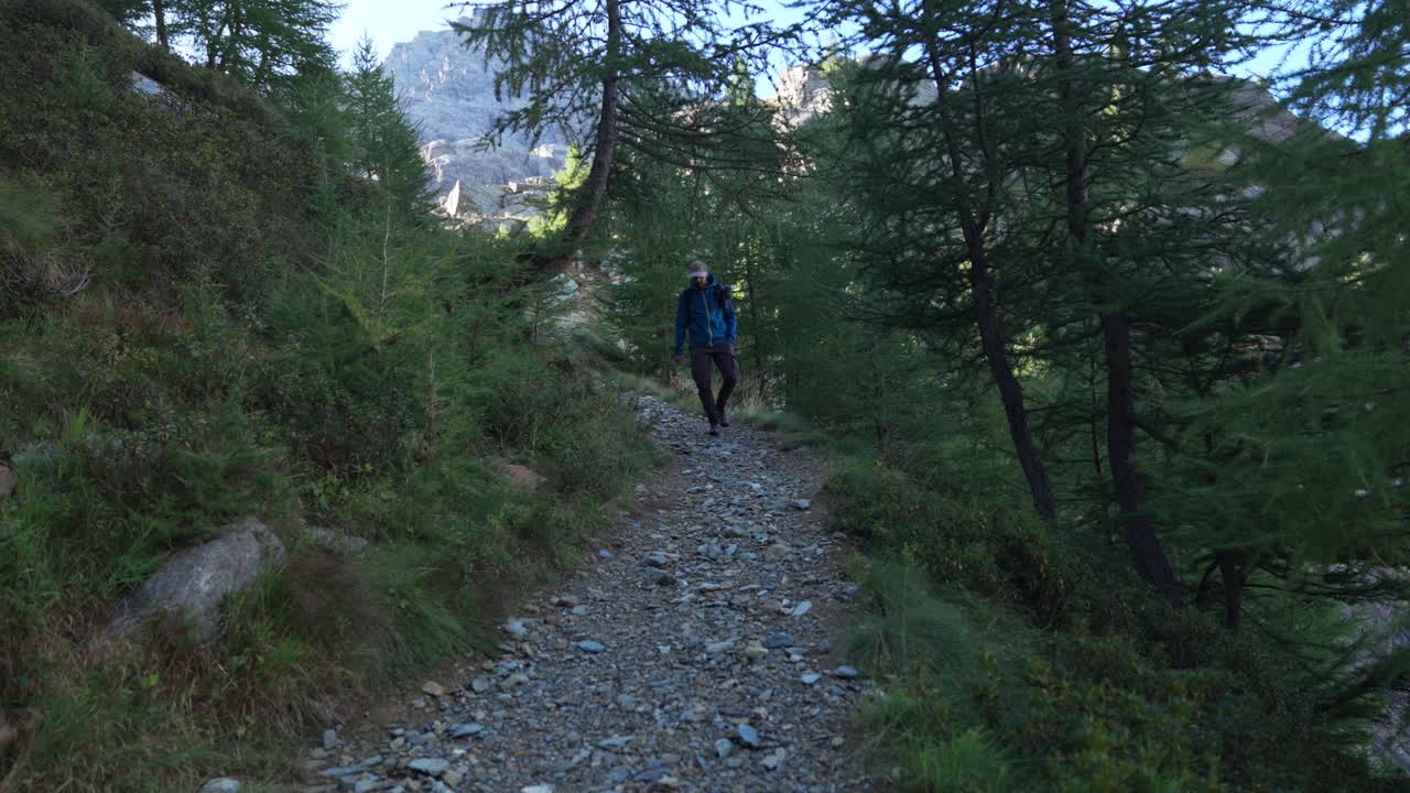 Slow motion front shot of man approaching camera in nature trail path, Valmalenco