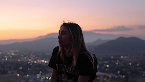 joven latina feliz frente a un paisaje urbano al atardecer con montañas en el fondo