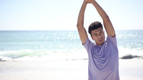 young biracial man stretches his arms on a sunny beach