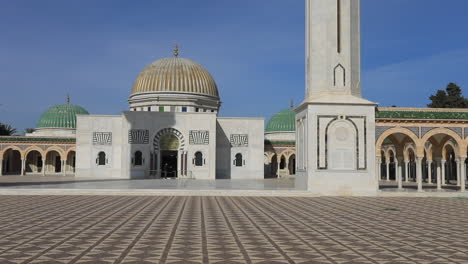 a large tunisian mausoleum with domes and arches stands under a bright blue sky