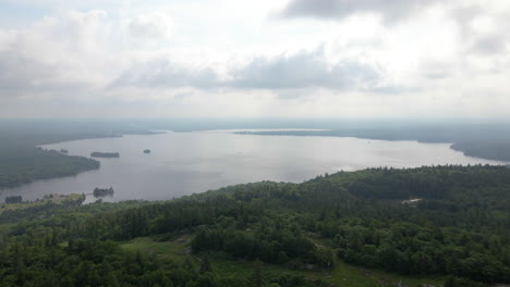aerial footage over thick green forest covered coastline approaching calm lake on overcast day. calabogie ontario