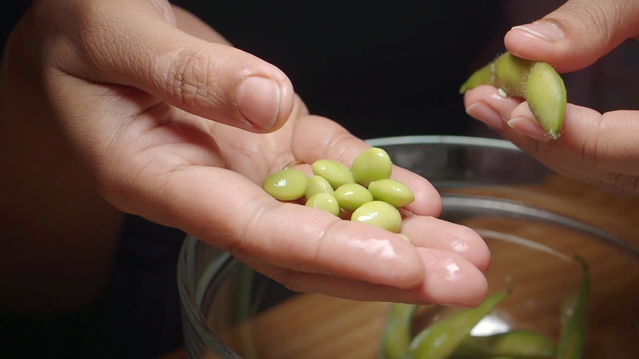Primo piano di mani che sbucciano fagioli edamame freschi e verdi.