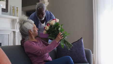 african american senior man giving gift box and flower bouquet to his wife at home