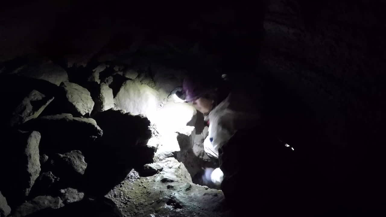 Female caver in white suit climbs up through tight cave restriction