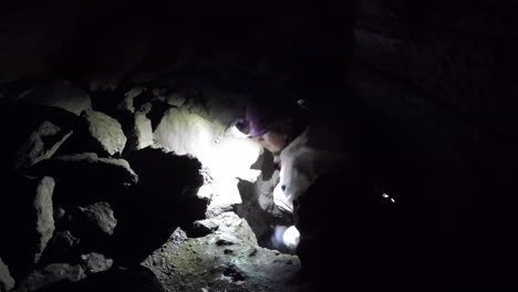 Female caver in white suit climbs up through tight cave restriction