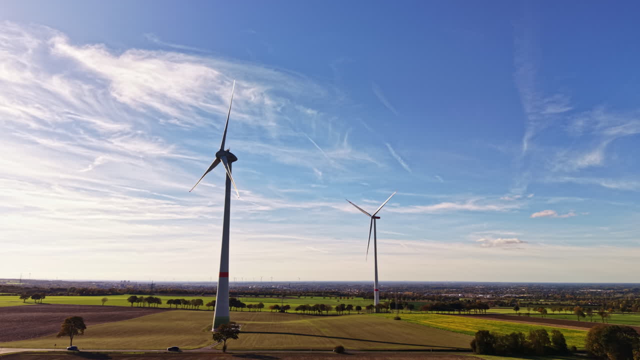 Wind turbines stand tall against a blue sky harnessing renewable energy in a vast green landscape with scattered clouds