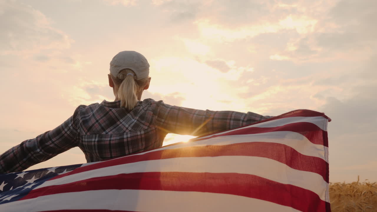 un hombre con una bandera americana en sus manos se para en un campo de trigo maduro