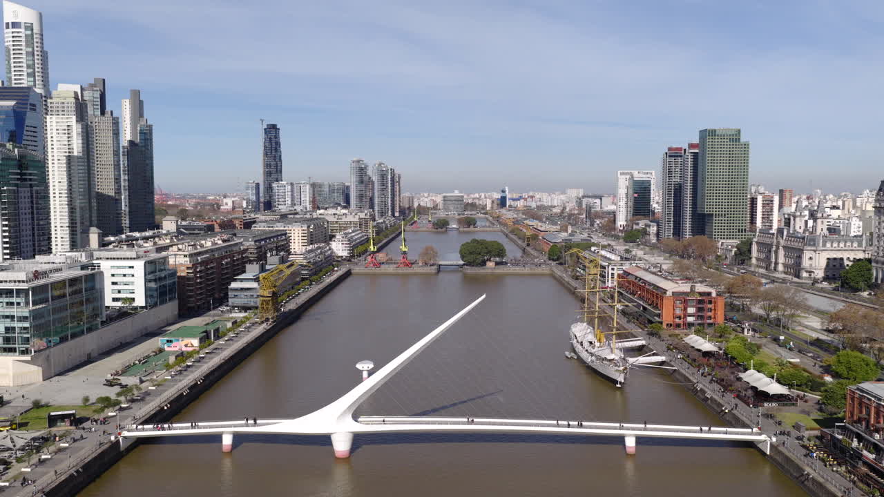 Aerial drone view of Puente de la Mujer bridge spanning canal with Buenos Aires skyline
