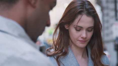 two millennial business colleagues standing on a street in london having a conversation and looking down at their smartphones, selective focus