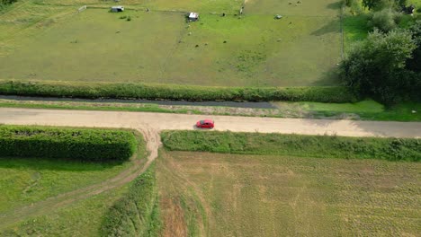 isolated red car driving on rural road in fields