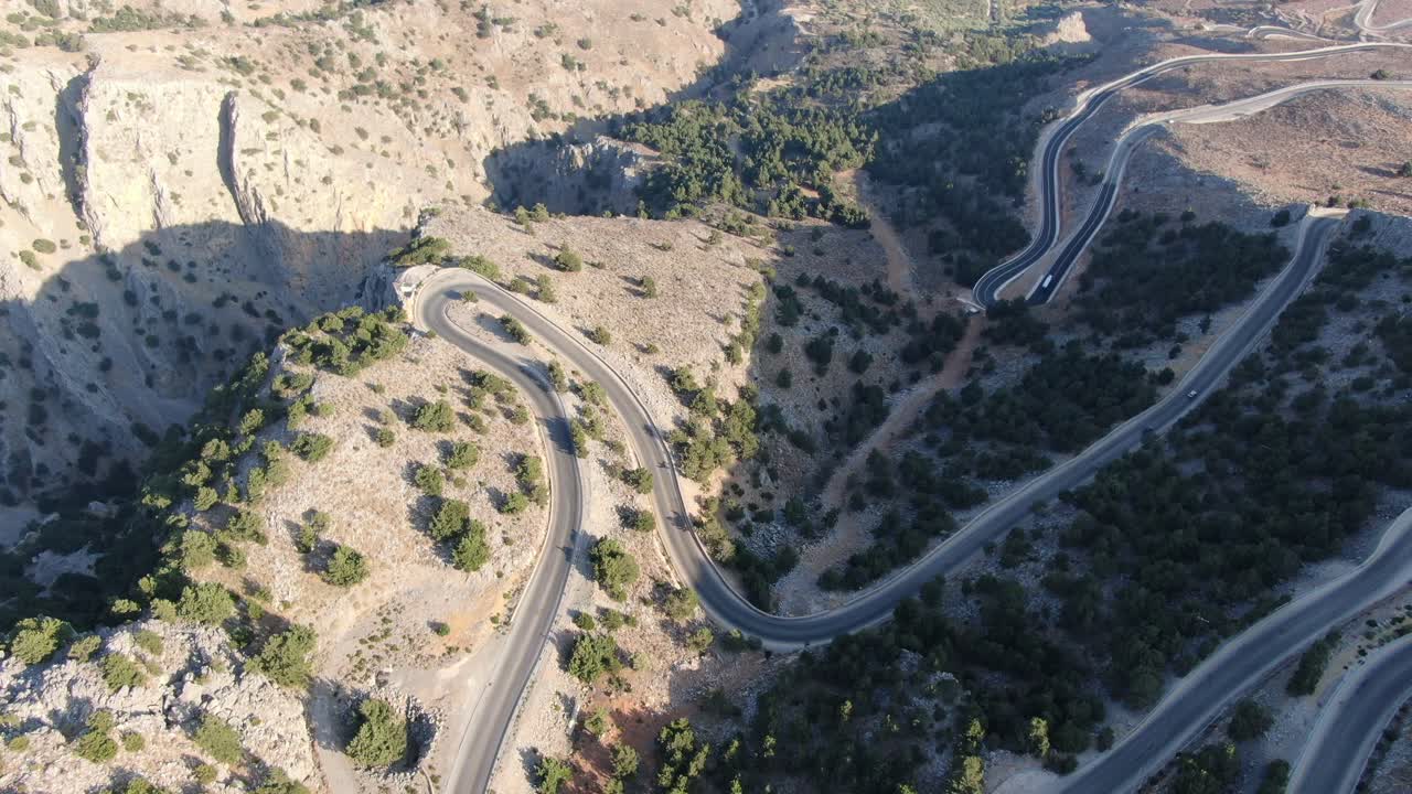 vista de avión no tripulado en grecia volando sobre una montaña marrón y verde con carretera de serpiente y mar en el horizonte en un día soleado