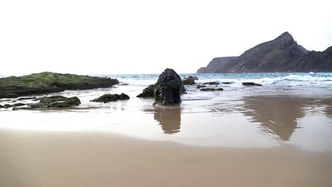 Relaxing-seascape-scene-view-of-sand-beach-front-with-islet,-rocks,-waves-foam-and-reflections