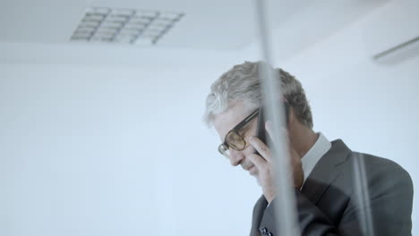 focused mature business leader walking in his office and speaking on phone