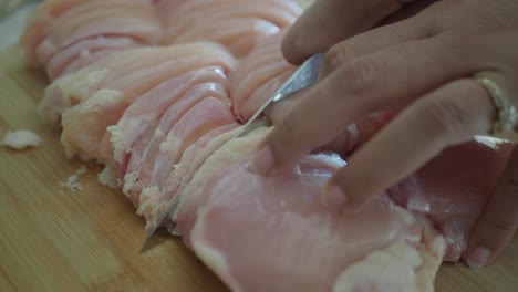 close up of a person cutting chicken breast with a knife on a cutting board.