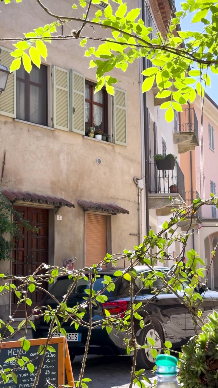 A car drives through a narrow cobblestone alleyway lined with historic pastel Italian architecture