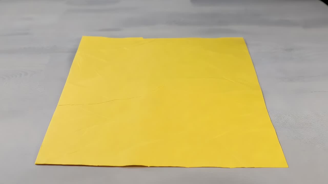 Compressione di un quadrato di carta gialla in una pallina accartocciata su un tavolo grigio chiaro, formando un motivo di pieghe