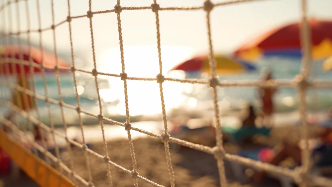 Una serena scena da spiaggia catturata attraverso una rete da pallavolo, che mostra ombrelloni colorati e bagnanti che si godono una giornata di sole in riva al mare.