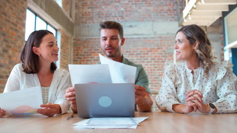 colegas de negocios masculinos y femeninos con computadora portátil y documentos que se reúnen en una oficina moderna