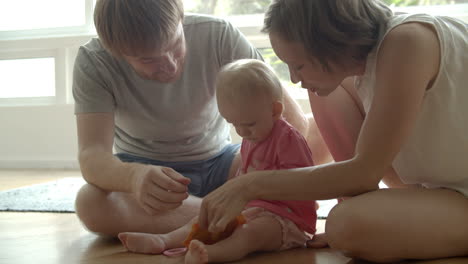 Lovely-baby-girl-sitting-on-floor-with-parents-and-playing